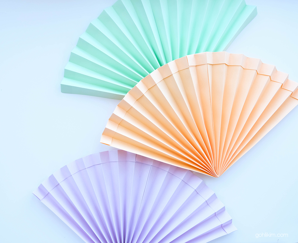 Handmade origami hand fan folded from A4 coloured paper, showing a sturdy no-glue design with reinforced double-layered edges.